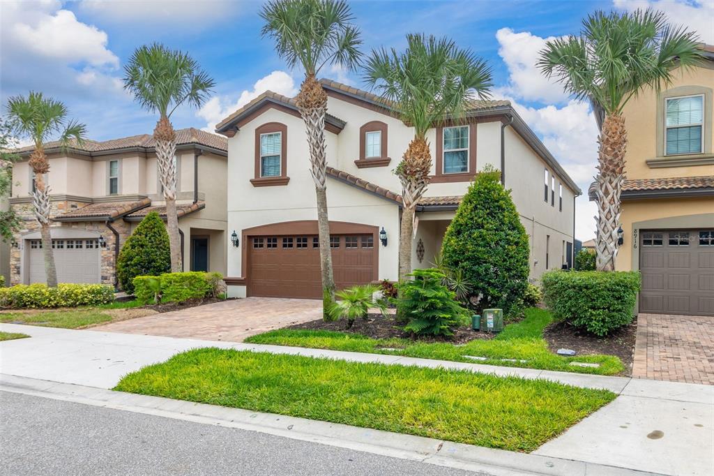A two-story suburban house with a brown garage door, palm trees, and a paved driveway — 8912 RHODES STREET, KISSIMMEE, FL