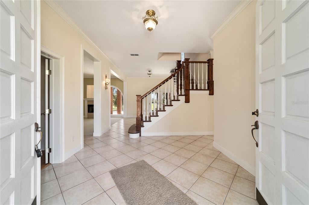 A tiled foyer features a wooden staircase with white balusters and a central light fixture — 1570 SE 73RD PLACE, OCALA, FL