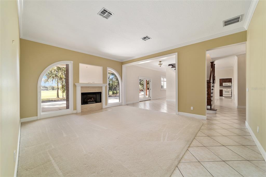 A carpeted living room features a fireplace, arched windows, and an adjacent tiled hallway — 1570 SE 73RD PLACE, OCALA, FL
