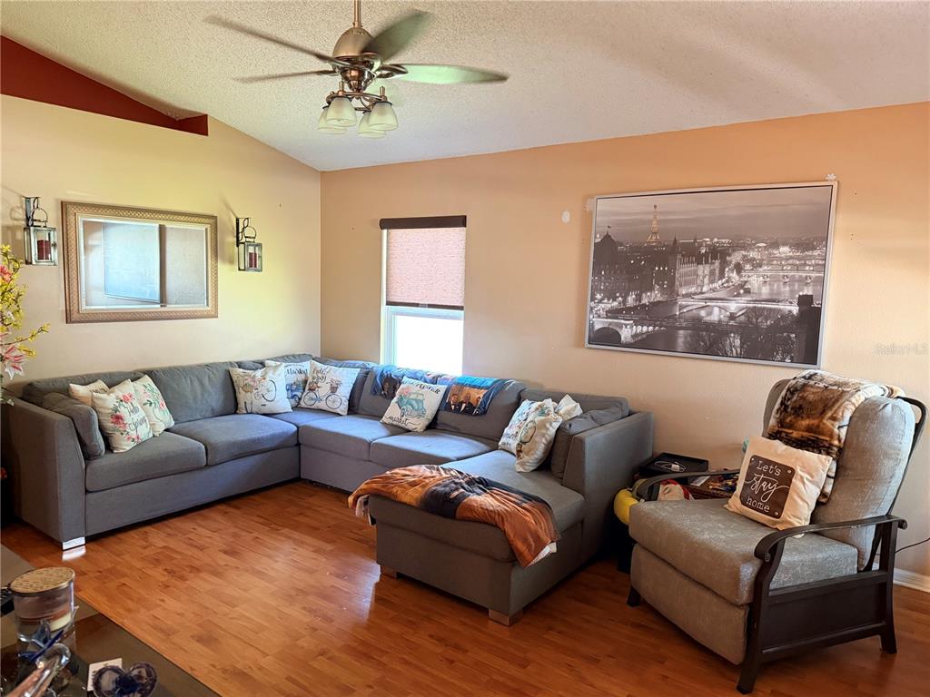 A living room features a large gray sectional sofa, an armchair, and wood-look flooring — 6224 TABOGI TRAIL, WESLEY CHAPEL, FL