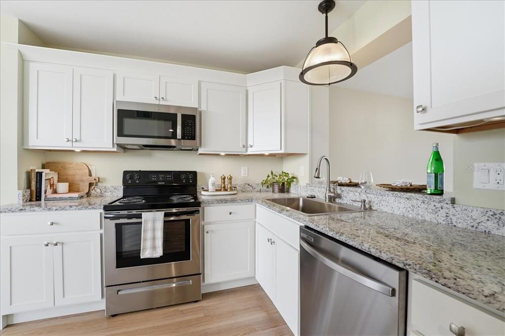A kitchen features white cabinets, stainless steel appliances, and granite countertops — 4550 PINEBROOK CIR UNIT 506, BRADENTON, FL