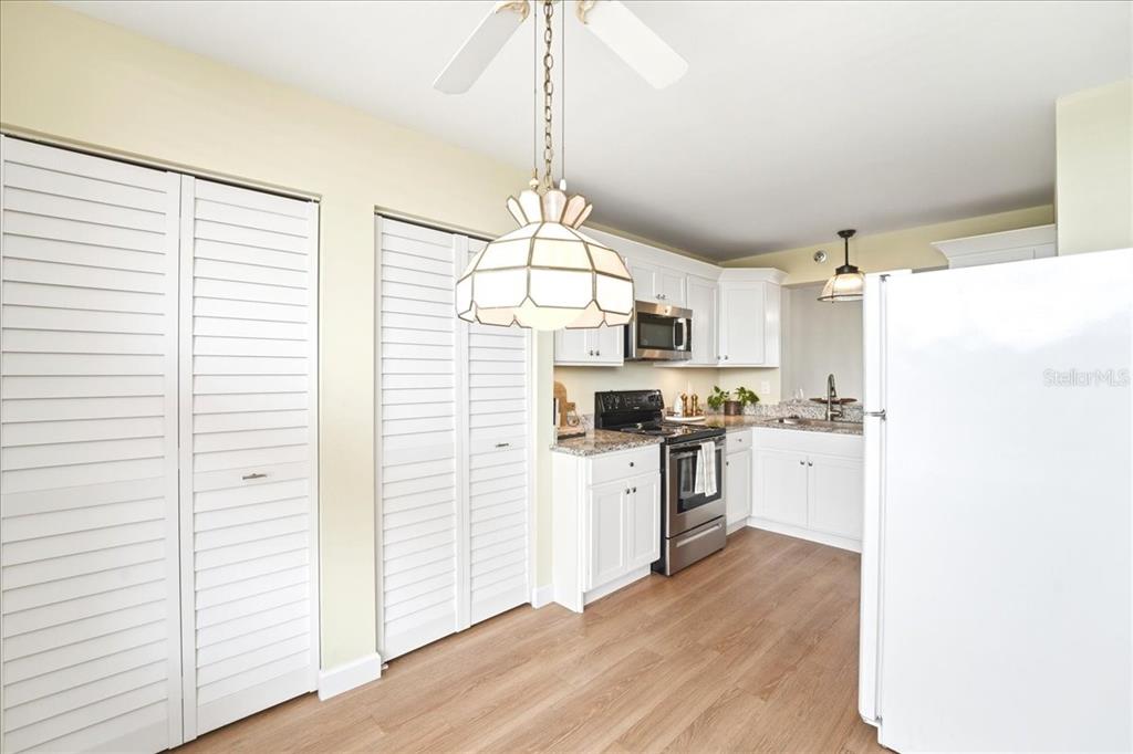 A kitchen features white cabinetry, stainless steel appliances, light wood flooring, and a pendant light — 4550 PINEBROOK CIR UNIT 506, BRADENTON, FL