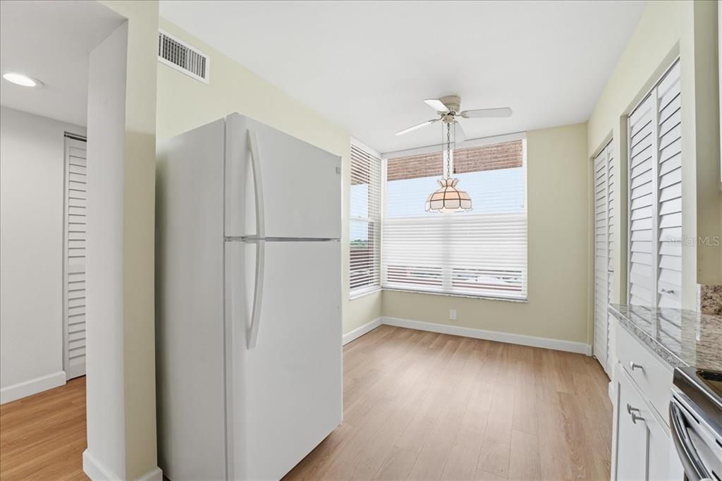 A kitchen area features a white refrigerator, light wood-look flooring, and a windowed breakfast nook — 4550 PINEBROOK CIR UNIT 506, BRADENTON, FL