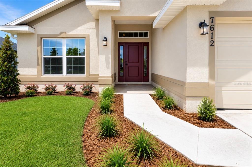 The exterior of a house features a red front door, tan stucco, and landscaping — 7612 BENT TREE LOOP, ST CLOUD, FL