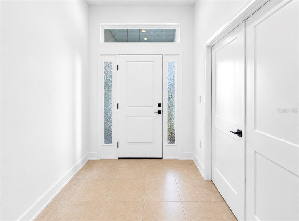 A bright entryway features a white front door with sidelights, a transom window, and tile flooring — 7612 BENT TREE LOOP, ST CLOUD, FL