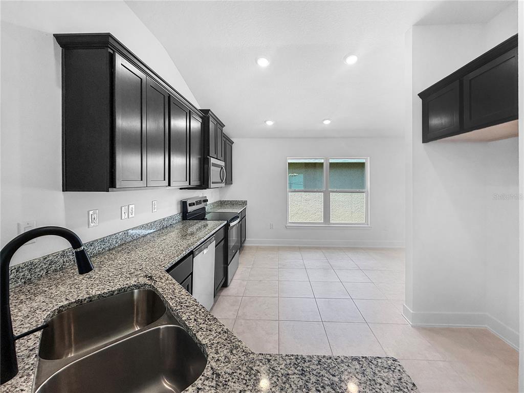 A kitchen features dark cabinets, granite countertops, stainless steel appliances, and light tile flooring — 7612 BENT TREE LOOP, ST CLOUD, FL