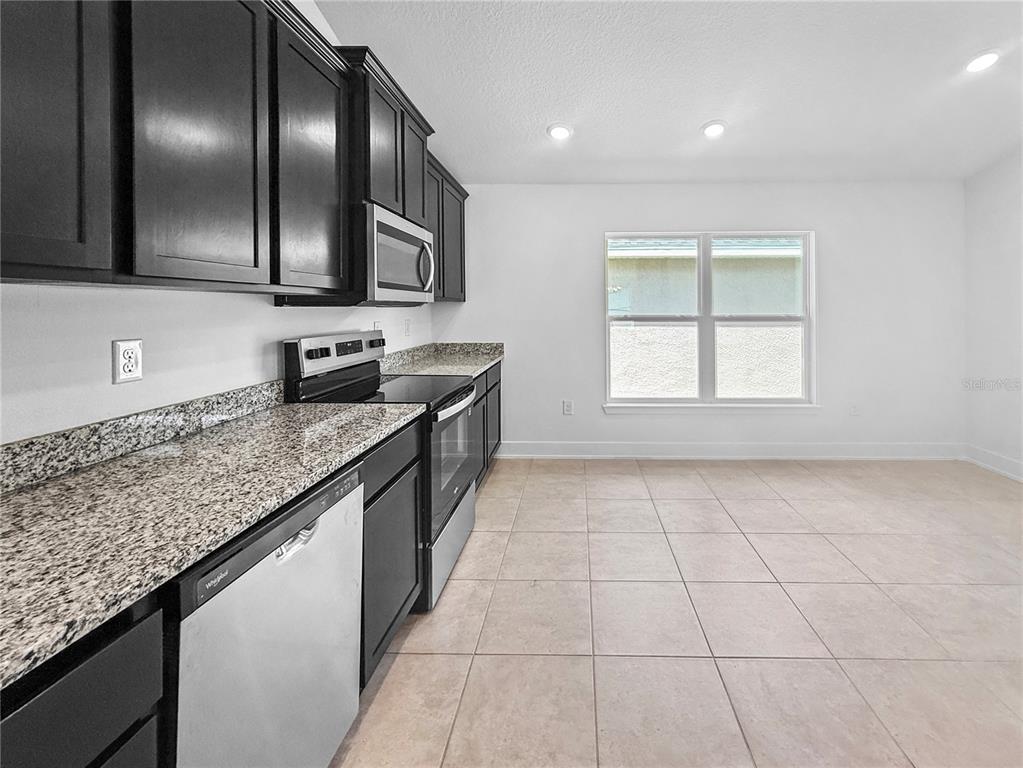 A kitchen features dark cabinets, granite countertops, stainless steel appliances, and light tile flooring — 7612 BENT TREE LOOP, ST CLOUD, FL