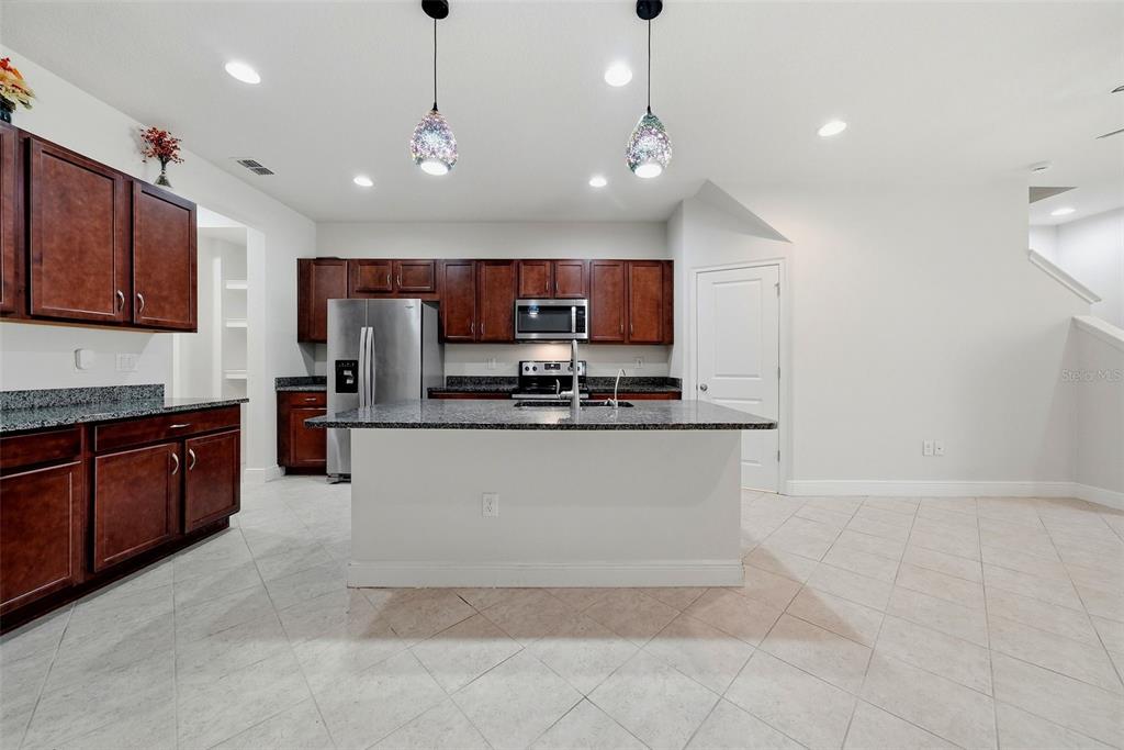 A kitchen with dark wood cabinets, granite countertops, a center island, and tile flooring — 11752 CAMBIUM CROWN DRIVE, RIVERVIEW, FL