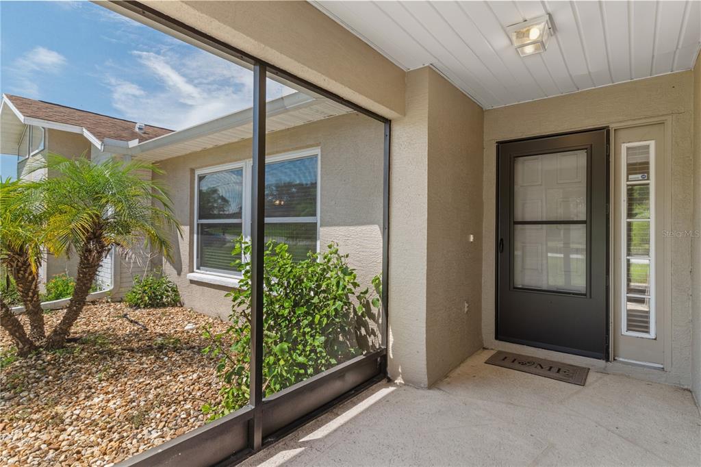 A covered entryway features a screen enclosure, a dark front door, and a gravel garden — 2285 GODFREY AVENUE, SPRING HILL, FL
