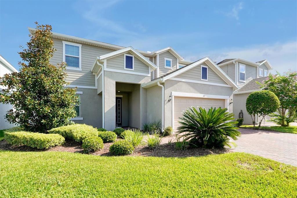 A two-story suburban house with beige siding, a two-car garage, and landscaped front yard — 1121 HENDON LOOP, DAVENPORT, FL