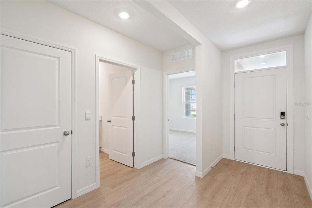 A bright entryway with light wood-look flooring, white doors, and a view into a bedroom — 847 SEAGROVE TRAIL, ST CLOUD, FL