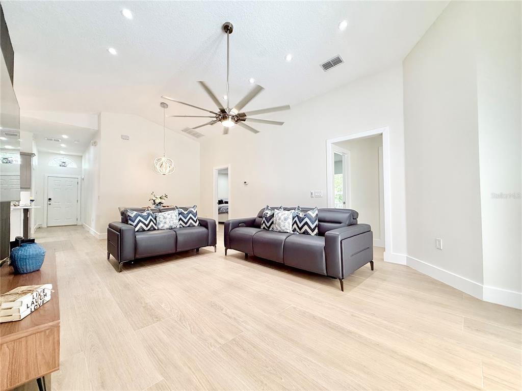 A living room features light wood-look flooring, two dark gray sofas, and a ceiling fan — 403 SANDY RIDGE DRIVE, DAVENPORT, FL