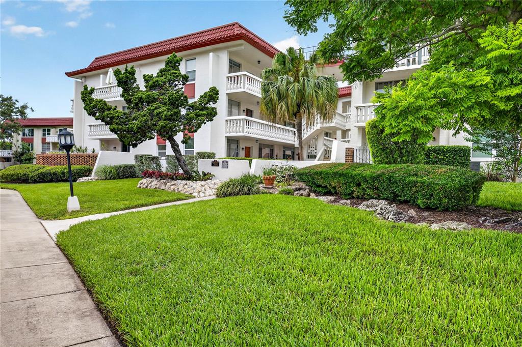 A multi-story apartment building with white balconies, a red tile roof, and landscaped front lawn — 2623 SEVILLE BOULEVARD UNIT 207, CLEARWATER, FL