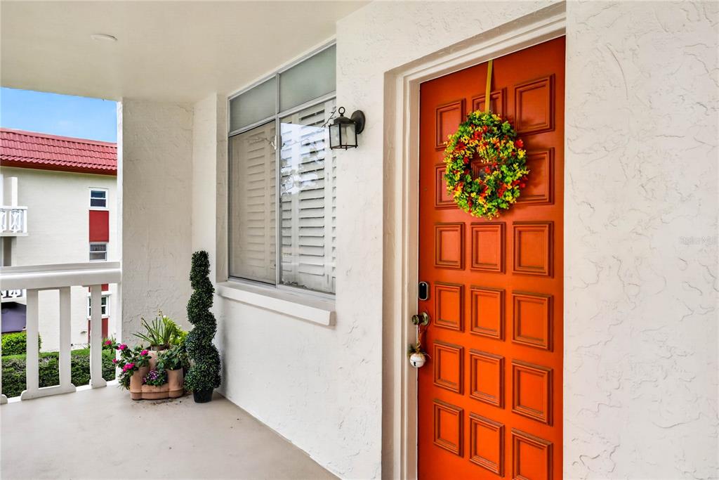 A bright orange front door with a wreath stands on a covered outdoor porch — 2623 SEVILLE BOULEVARD UNIT 207, CLEARWATER, FL