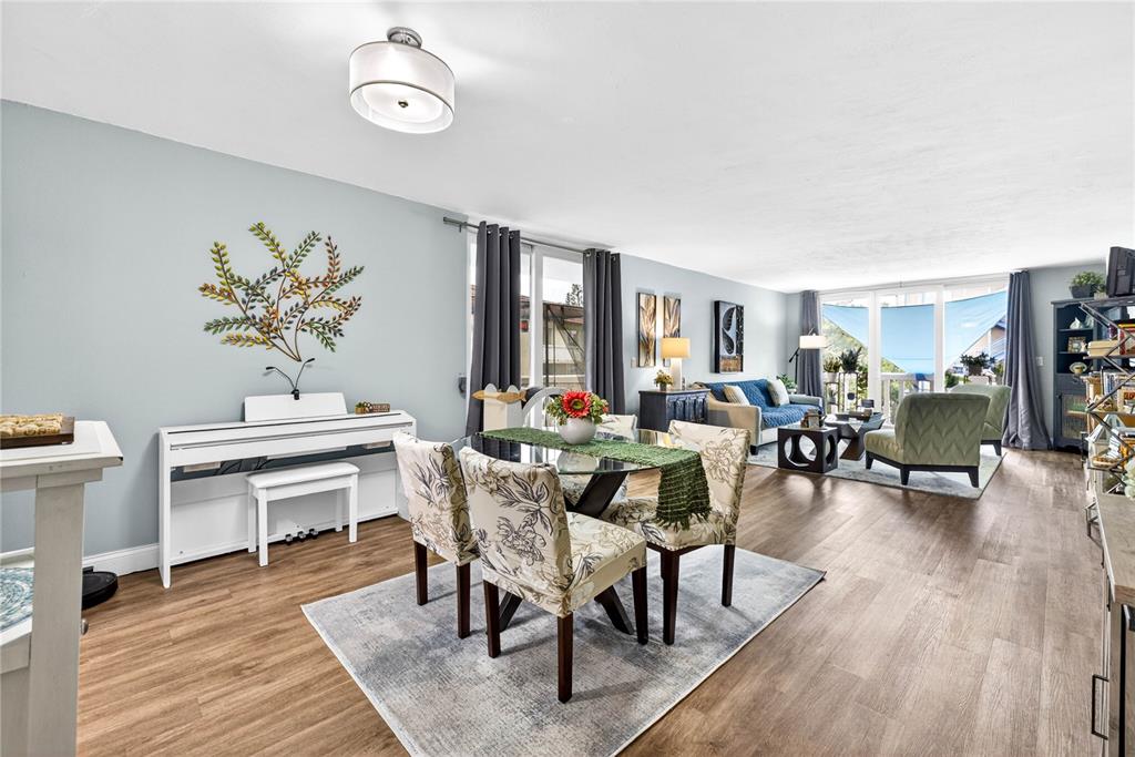 A living and dining area with wood-look flooring, a glass-top table, and a white piano — 2623 SEVILLE BOULEVARD UNIT 207, CLEARWATER, FL
