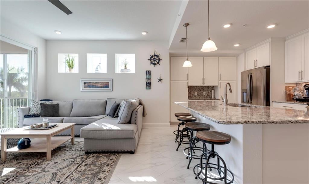 An open-concept living room and kitchen featuring a gray sectional sofa and granite island seating — 395 ARUBA CIRCLE UNIT 203, BRADENTON, FL