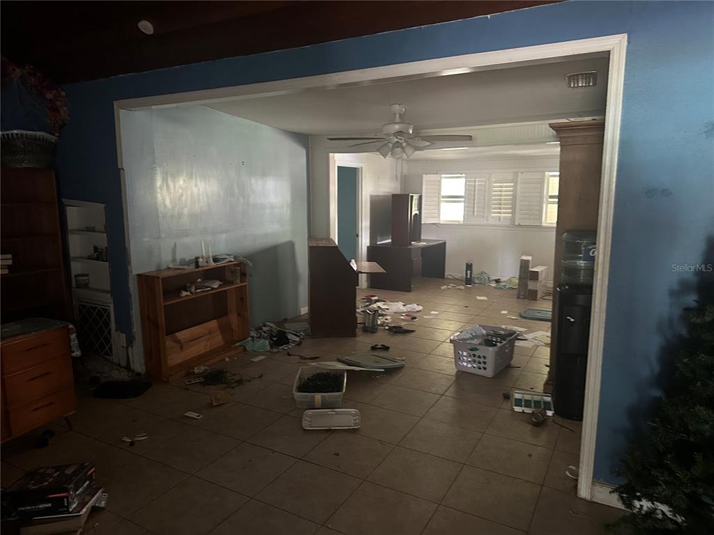 An interior view shows a tiled room with a ceiling fan and scattered household items — 1245 35TH AVENUE, VERO BEACH, FL