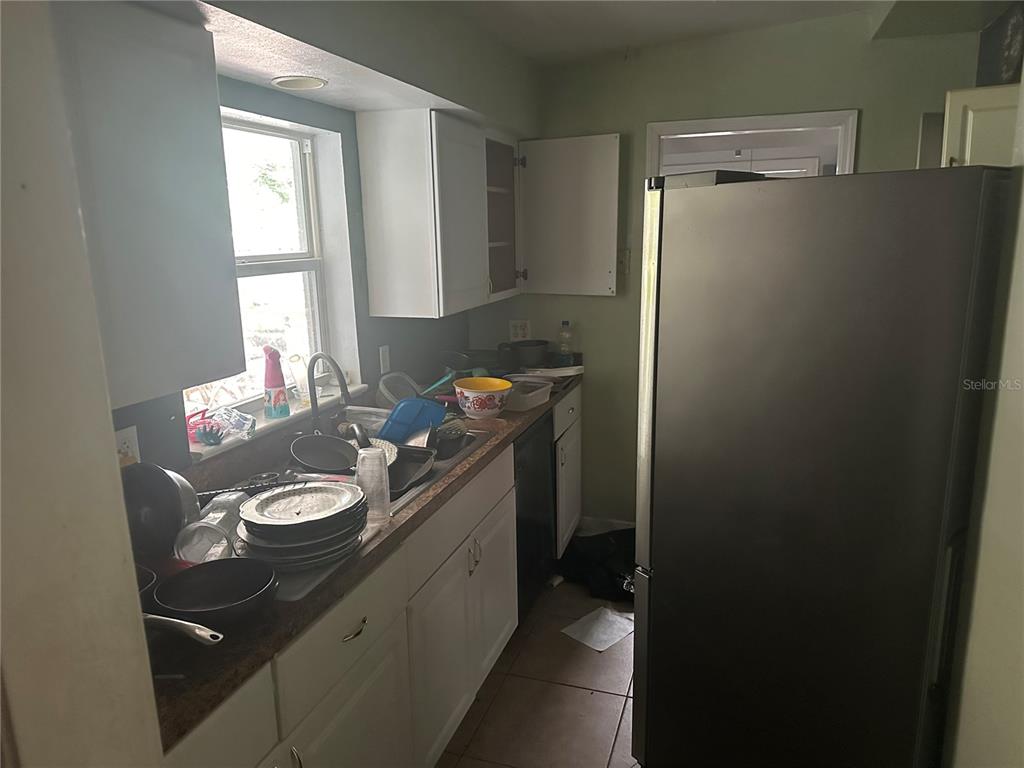 A kitchen features white cabinets, a stainless steel refrigerator, and a sink filled with dishes — 1245 35TH AVENUE, VERO BEACH, FL