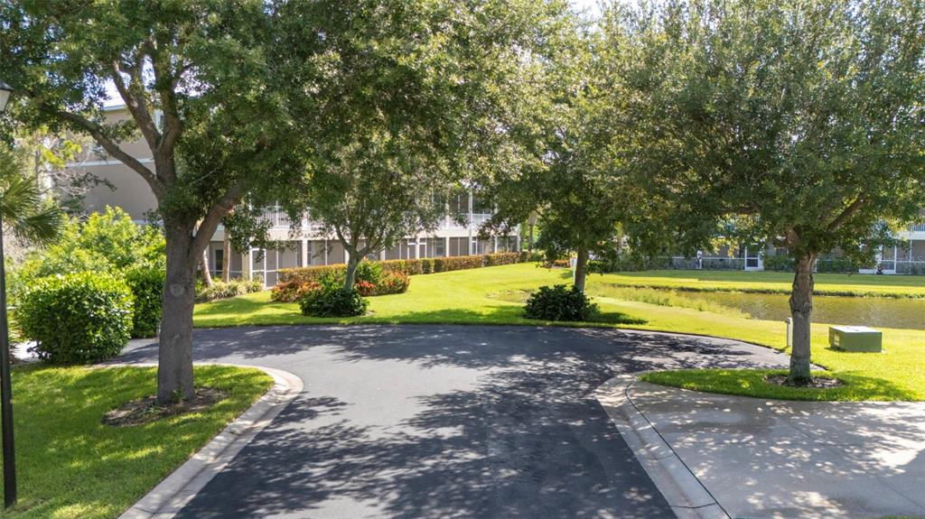 A paved driveway leads toward a multi-story apartment building surrounded by trees and a pond — 10307 CORAL LANDINGS LANE UNIT 11, PLACIDA, FL