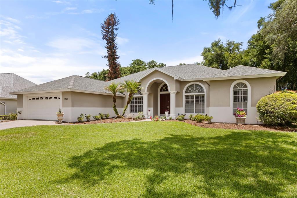 A single-story suburban house with a two-car garage, arched entryway, and a large front lawn — 1521 EDGEWATER DRIVE, MOUNT DORA, FL