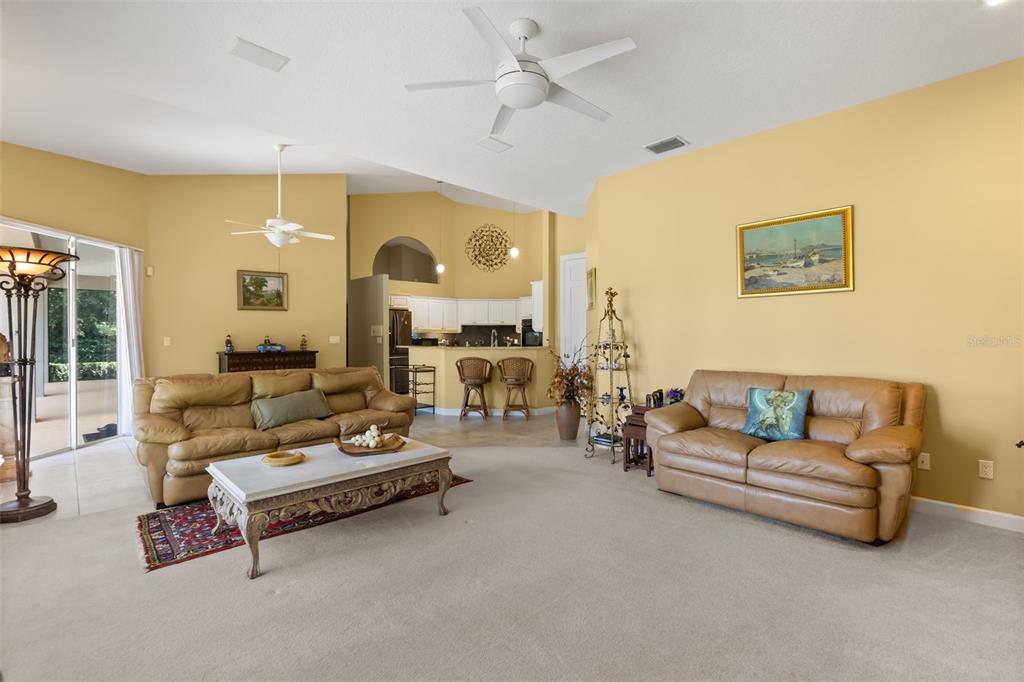 A living room with tan walls, beige carpet, two leather sofas, and an open kitchen — 1521 EDGEWATER DRIVE, MOUNT DORA, FL