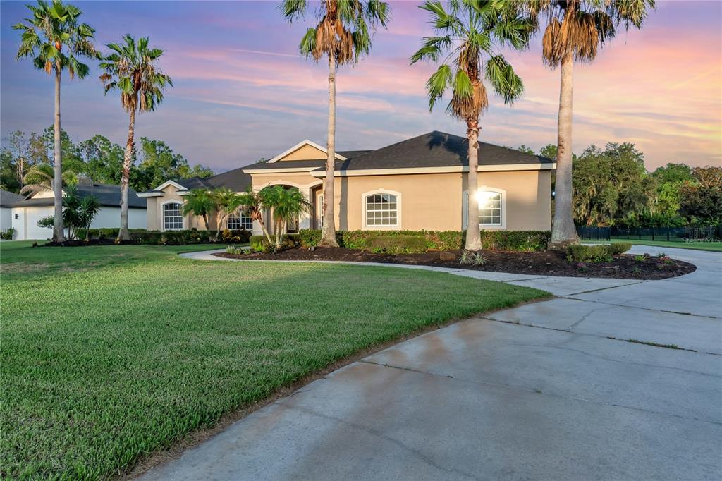 A single-story beige house with a concrete driveway and palm trees under a sunset sky — 15425 29TH LANE E, PARRISH, FL