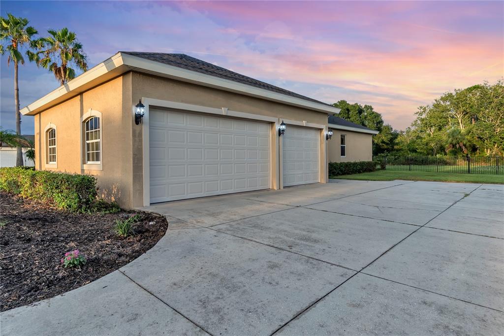 A tan stucco garage with two white doors and a concrete driveway at sunset — 15425 29TH LANE E, PARRISH, FL