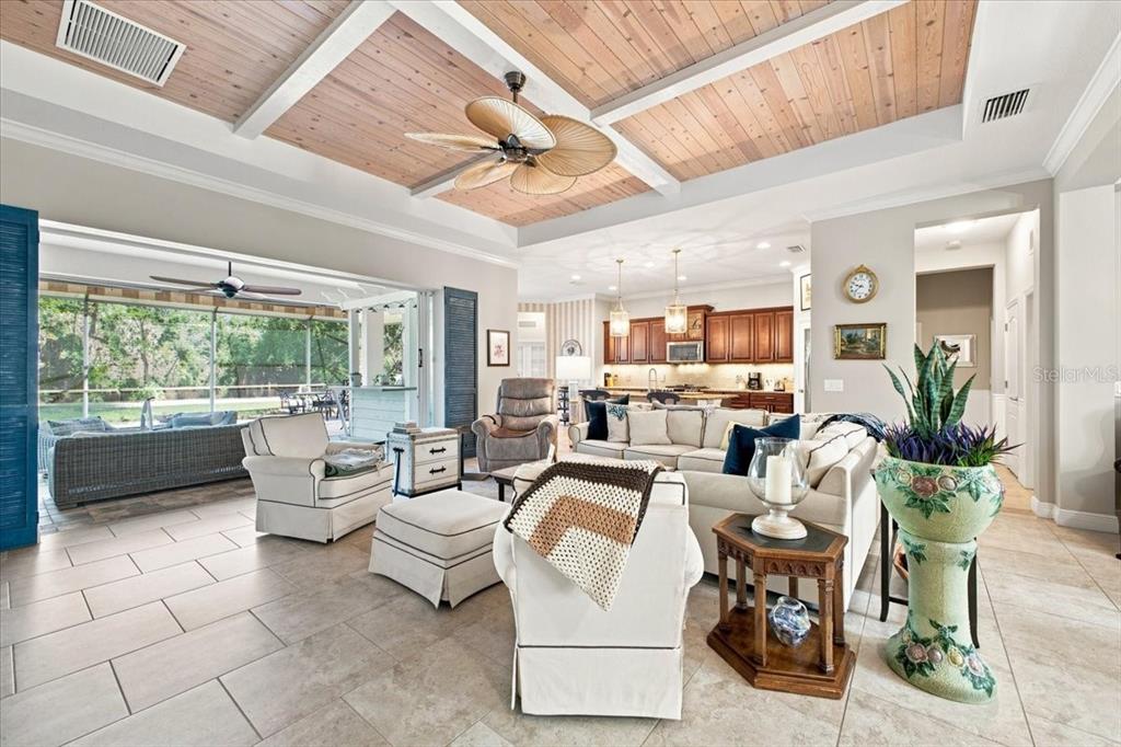 A living room with a coffered wood ceiling opens to a screened-in outdoor patio area — 4704 SENECA PARK TRAIL, BRADENTON, FL