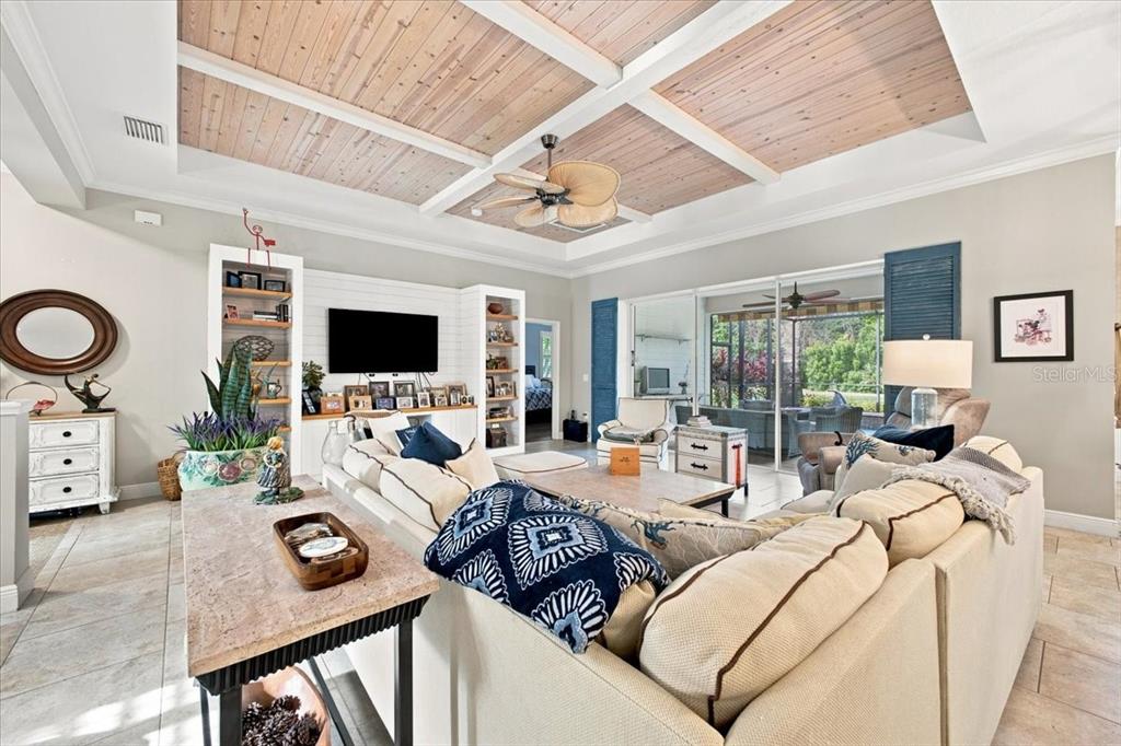 A living room features a coffered wood-paneled ceiling, a large sectional sofa, and built-in shelving — 4704 SENECA PARK TRAIL, BRADENTON, FL