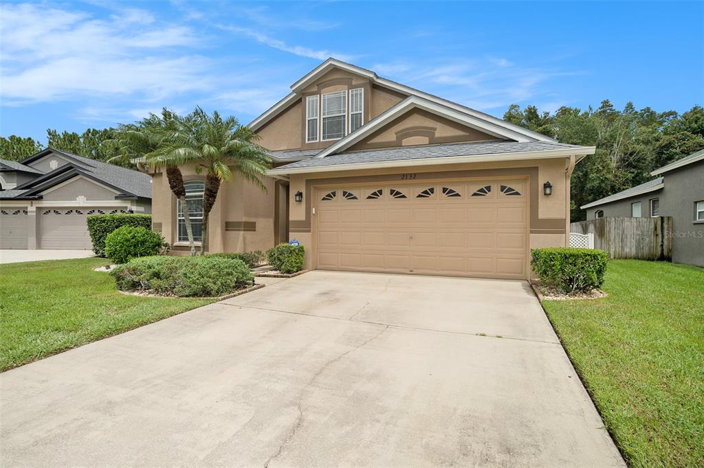 A tan suburban house with a two-car garage, a palm tree, and a concrete driveway — 2132 RENSSELAER DRIVE, WESLEY CHAPEL, FL