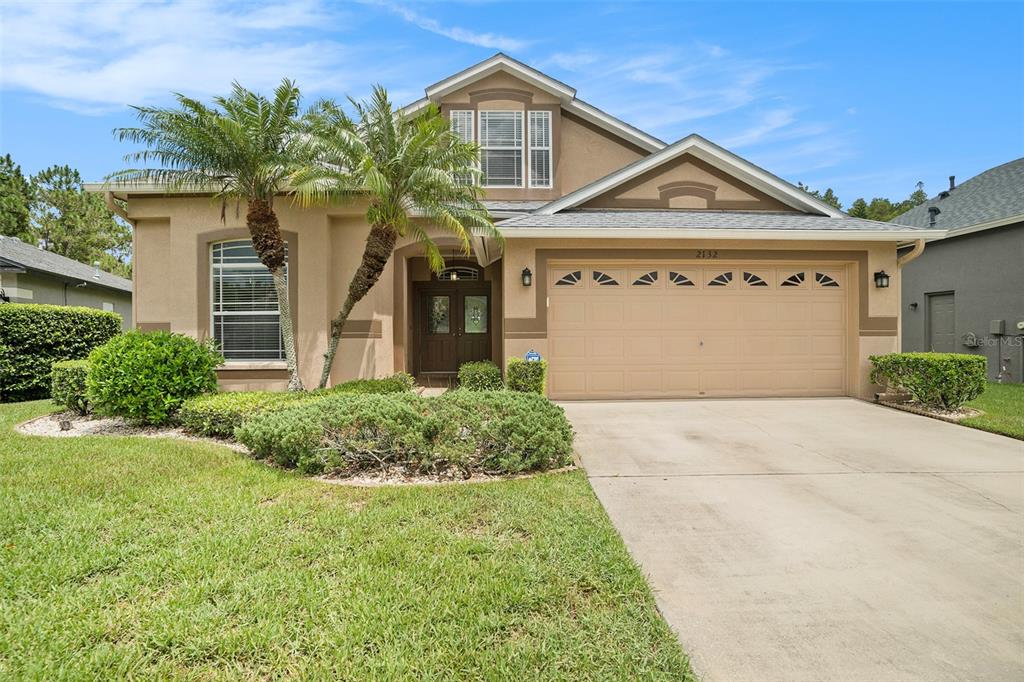 A two-story tan stucco house with a two-car garage and two palm trees in front — 2132 RENSSELAER DRIVE, WESLEY CHAPEL, FL