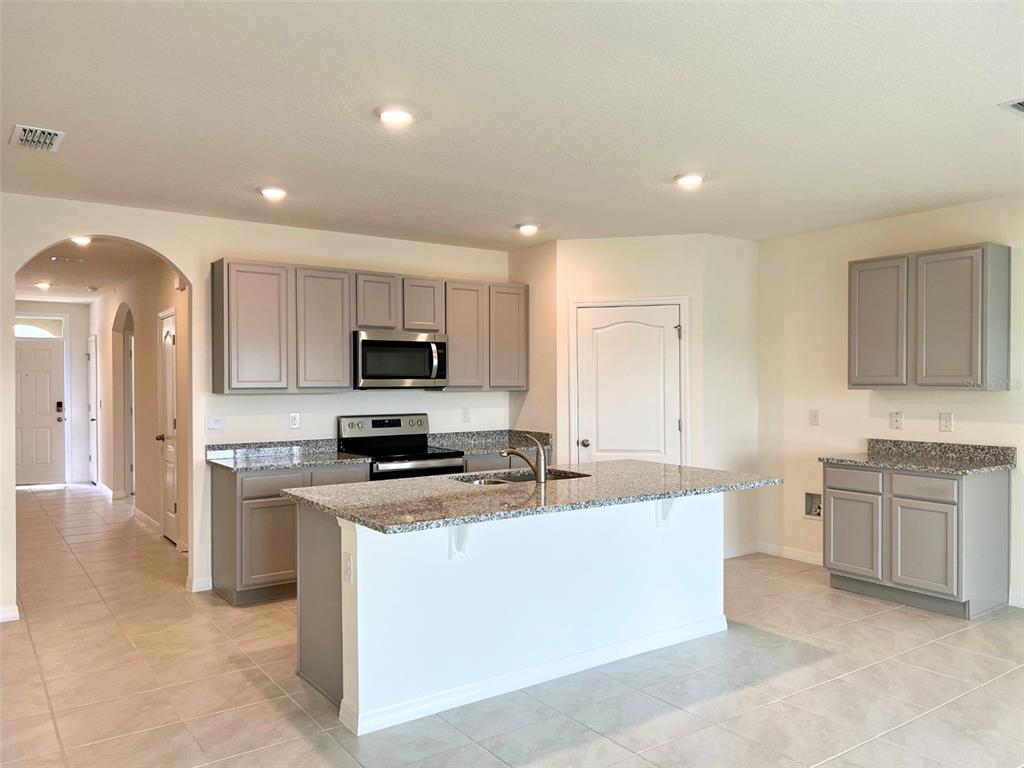 A kitchen features gray cabinets, granite countertops, a central island, and light-colored tile flooring — 2877 SUNRIDGE LOOP, ST CLOUD, FL