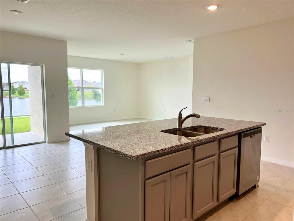 A kitchen island with a granite countertop and sink sits in an open-concept living space — 2877 SUNRIDGE LOOP, ST CLOUD, FL