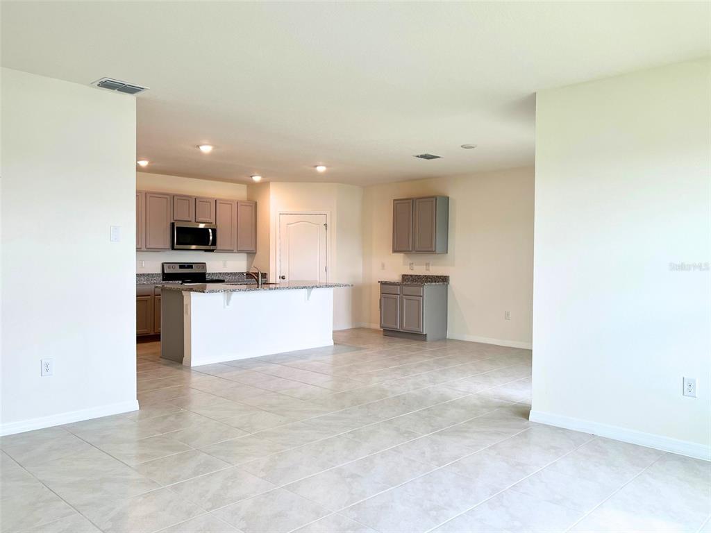 An open-concept kitchen features gray cabinets, granite countertops, and light-colored tile flooring — 2877 SUNRIDGE LOOP, ST CLOUD, FL