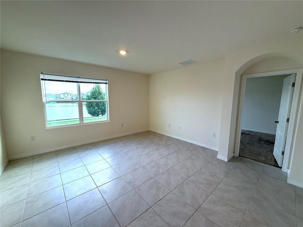 An empty room features light-colored tile flooring, beige walls, and a window overlooking a lake — 2877 SUNRIDGE LOOP, ST CLOUD, FL