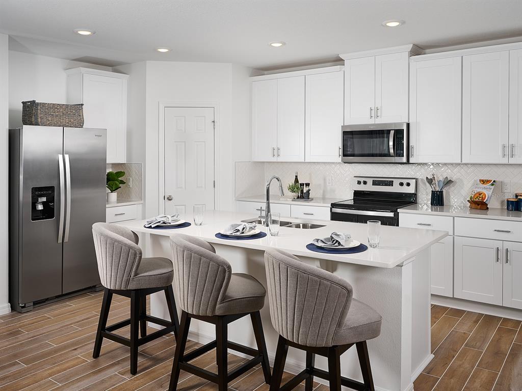 A modern kitchen features white cabinets, stainless steel appliances, a center island, and bar stools — 2202 SAGELAND WAY, BARTOW, FL