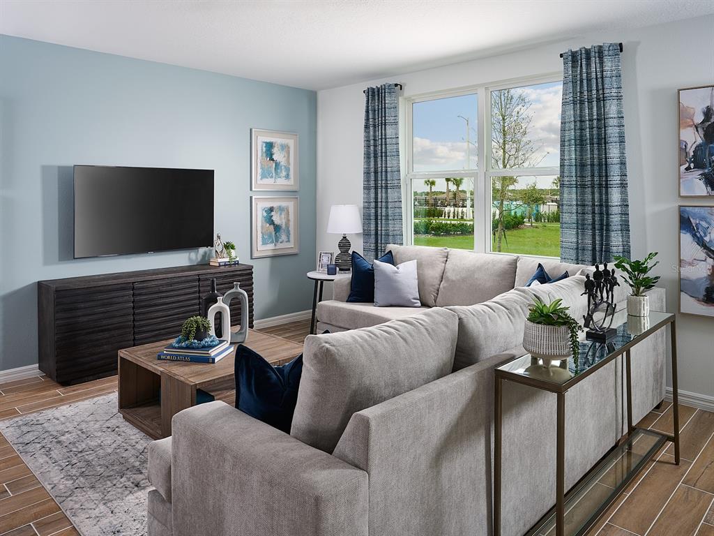 A living room features a grey sectional sofa, a dark wood media console, and blue accents — 2202 SAGELAND WAY, BARTOW, FL