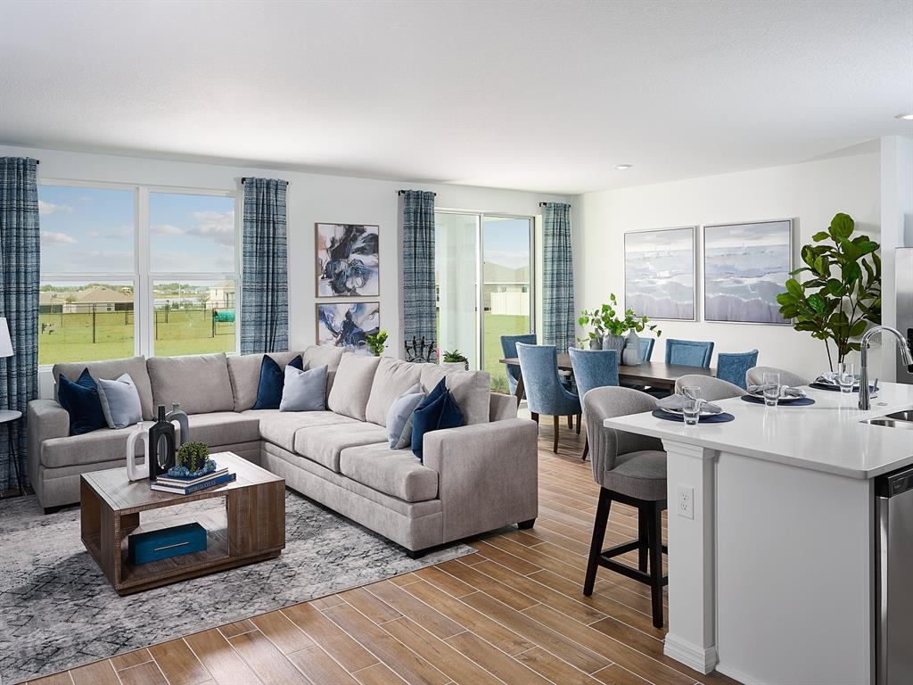 An open-concept living and dining area features a sectional sofa, kitchen island, and tile flooring — 2202 SAGELAND WAY, BARTOW, FL