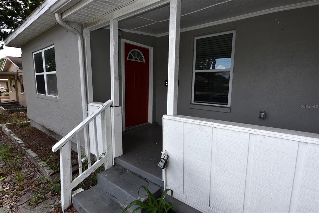 A gray house exterior features a red front door, white porch railing, and concrete steps — 4642 10TH AVENUE S, ST PETERSBURG, FL