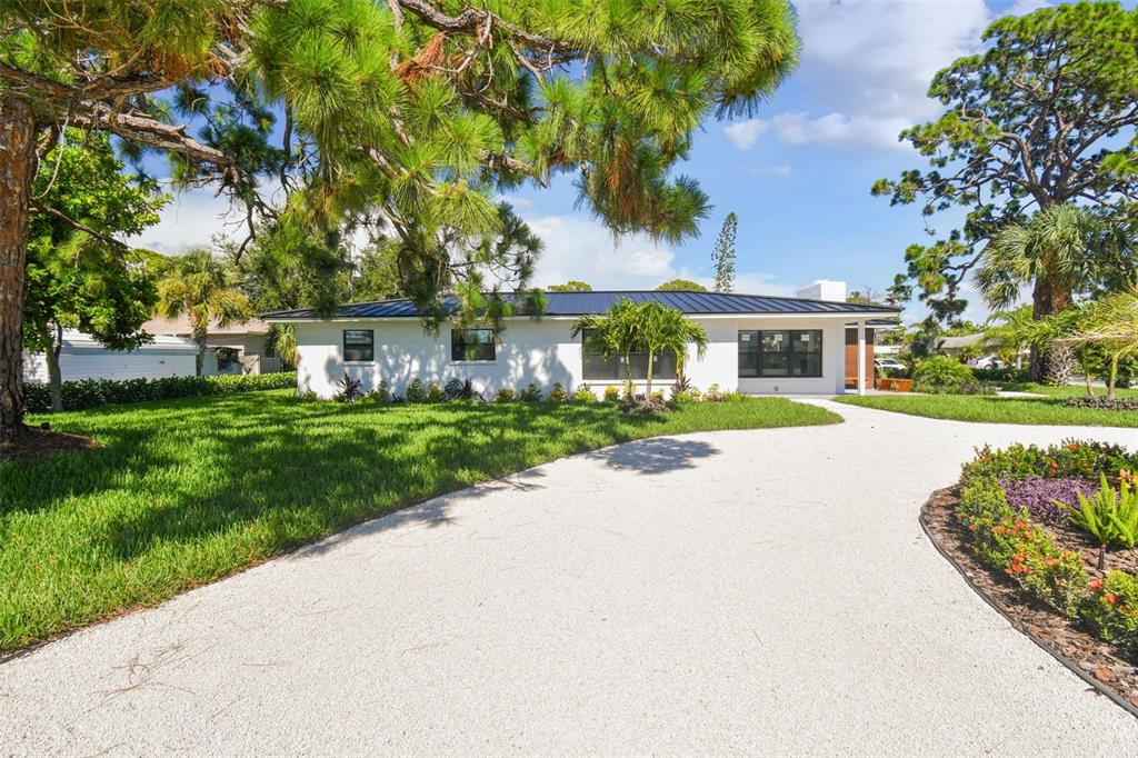 A white single-story house with a black metal roof sits behind a gravel driveway — 301 AURORA STREET E, VENICE, FL