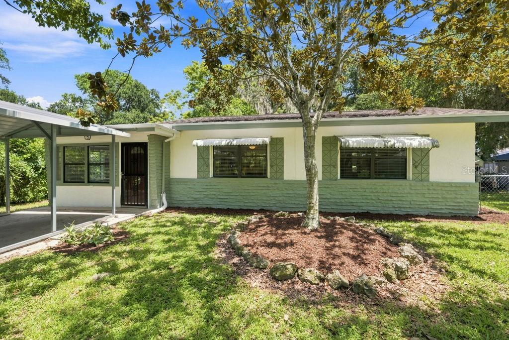 A single-story house with a metal carport and a large tree in the front yard — 7810 CHAPEL AVENUE, PORT RICHEY, FL