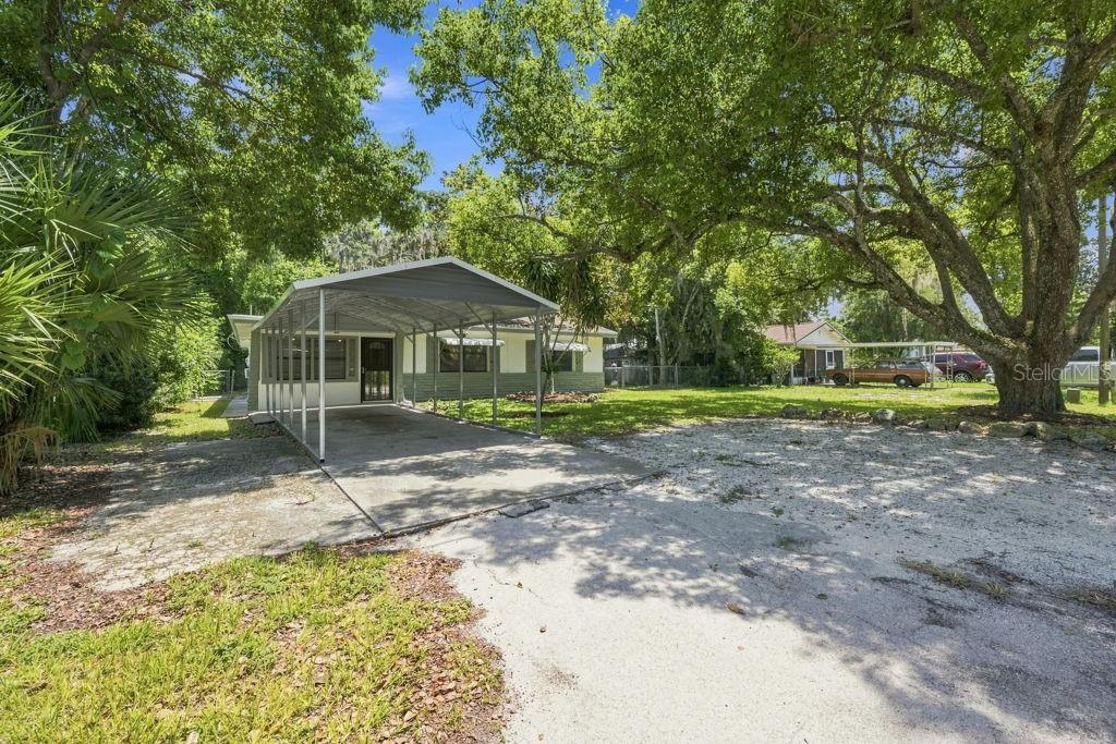 A single-story house with a metal carport, green brick siding, and a large front yard — 7810 CHAPEL AVENUE, PORT RICHEY, FL