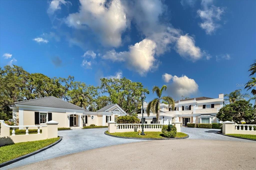 A large, multi-story estate with a paved circular driveway and lush landscaping under a blue sky — 236 SAINT JAMES PARK, OSPREY, FL