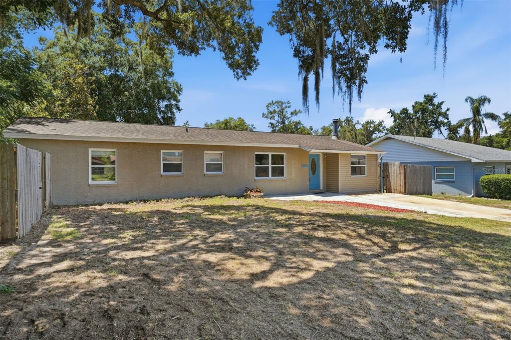 A single-story house with a tan stucco exterior, a blue front door, and a concrete driveway — 3104 GARDEN ROAD, EUSTIS, FL