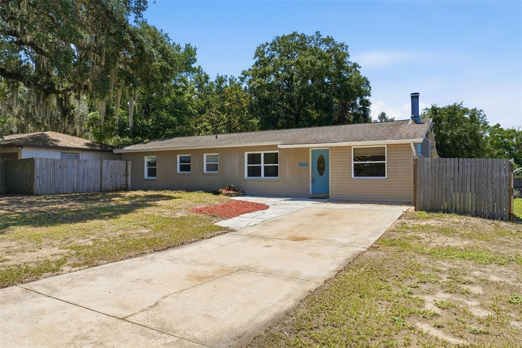 A single-story house with a tan exterior, a concrete driveway, and a wooden fence — 3104 GARDEN ROAD, EUSTIS, FL
