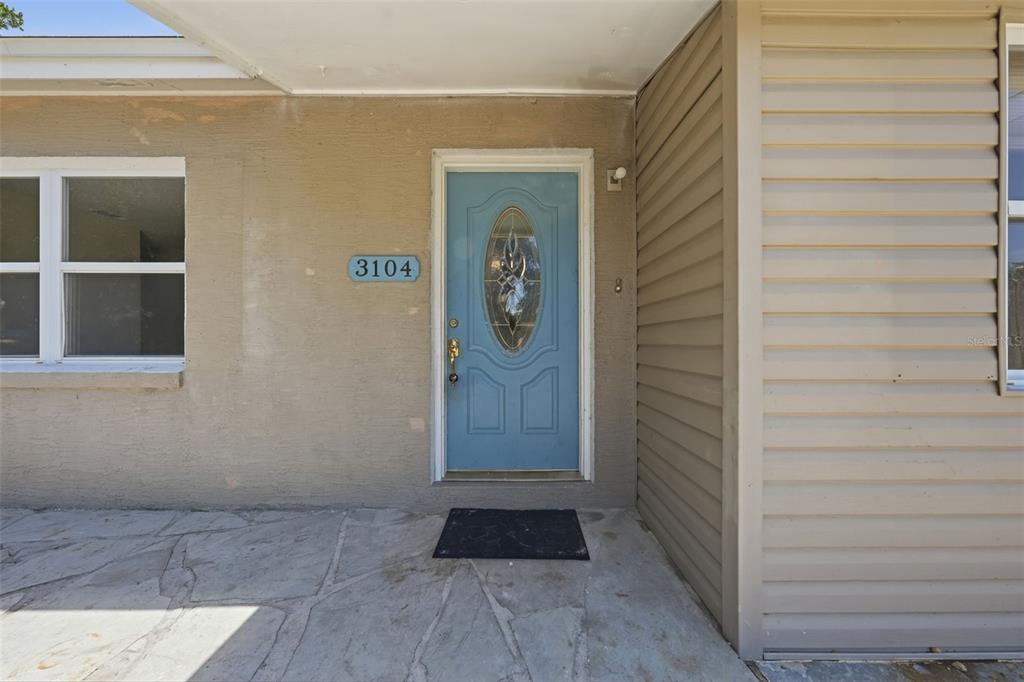 A blue front door with an oval glass insert is centered on a tan exterior wall — 3104 GARDEN ROAD, EUSTIS, FL