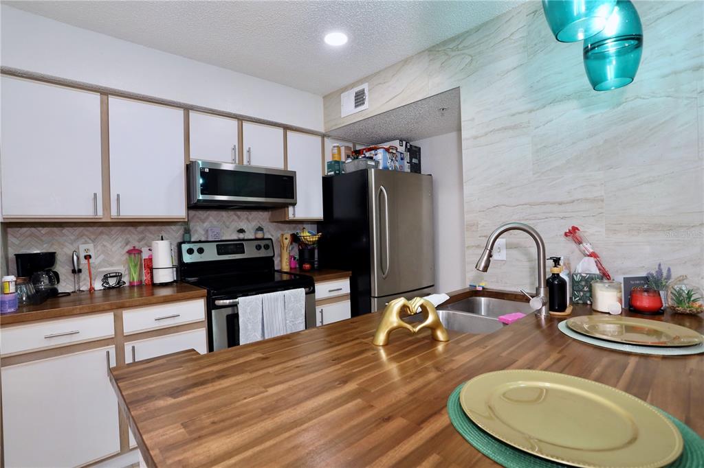 A kitchen features white cabinets, wood countertops, stainless steel appliances, and a tile backsplash — 2217 GRAND CAYMAN COURT UNIT 1236, KISSIMMEE, FL
