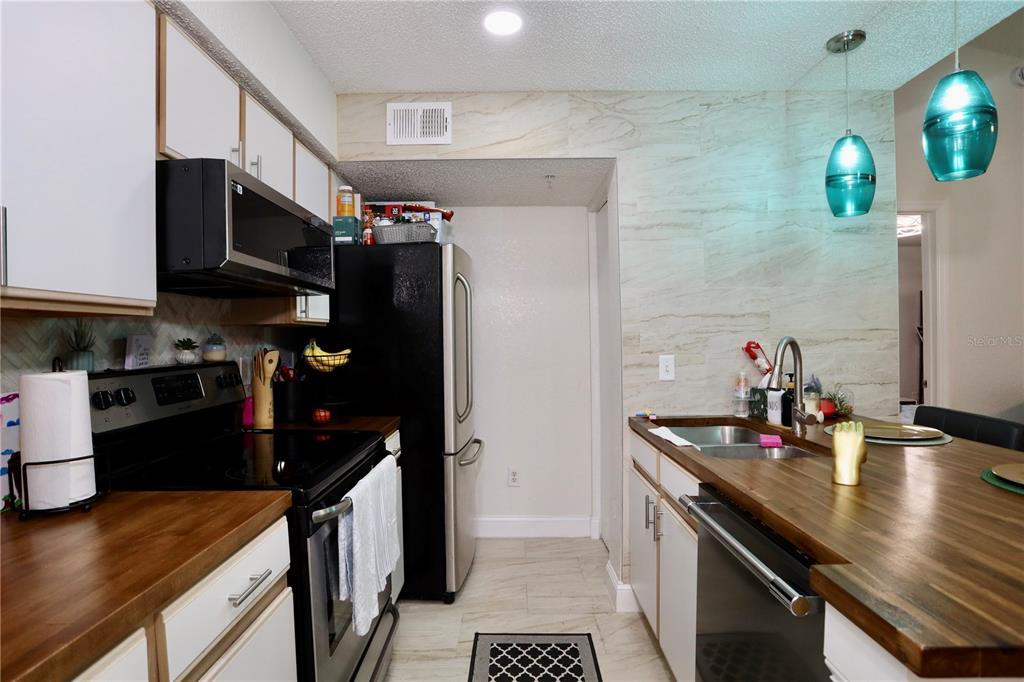 A kitchen features white cabinets, wood countertops, stainless steel appliances, and two blue pendant lights — 2217 GRAND CAYMAN COURT UNIT 1236, KISSIMMEE, FL