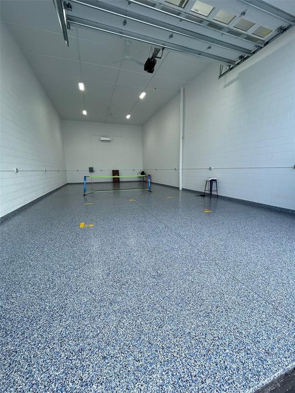 A spacious garage with white block walls, a speckled epoxy floor, and a pickleball net — 5237 TAYLOR ROAD UNIT E9, PUNTA GORDA, FL