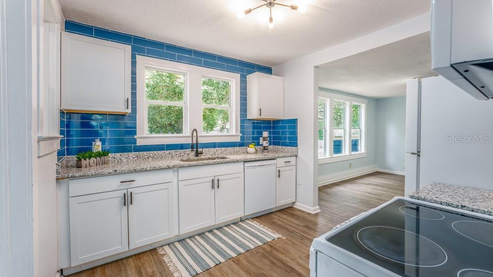 A kitchen features white cabinets, granite countertops, blue subway tile backsplash, and wood-look flooring — 912 E CAROLINA AVE, DELAND, FL
